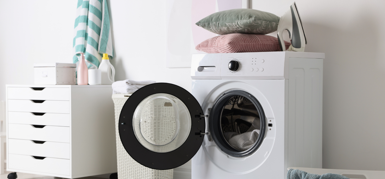 Machine à laver avec des oreillers colorés posés sur le dessus, prête pour un cycle de lavage.