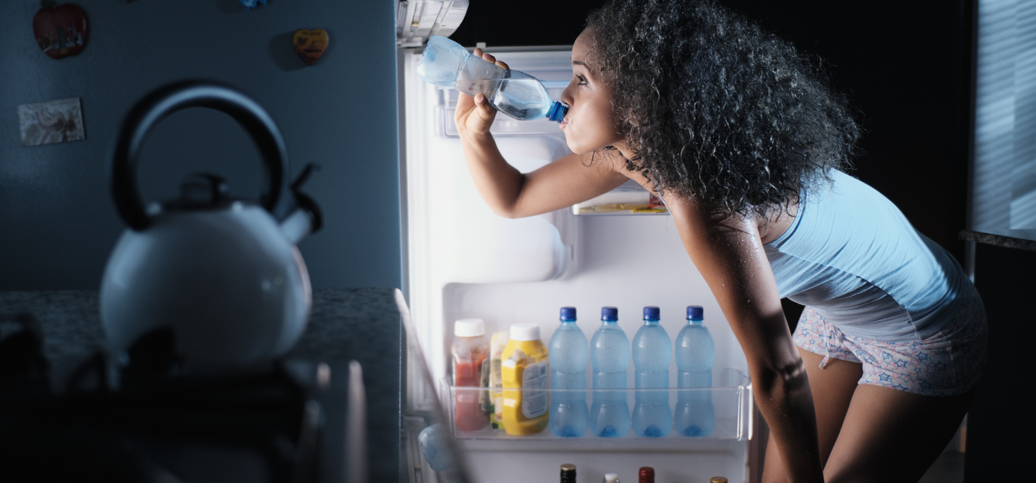Femme buvant de l'eau devant son réfrigérateur la nuit pour se réhydrater